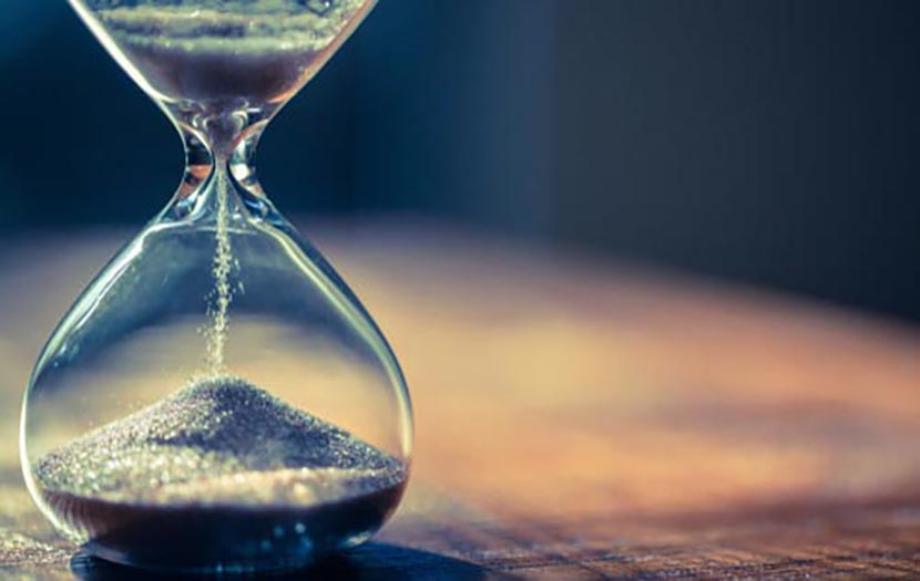 Sand running through the bulbs of an hourglass measuring the passing time in a countdown to a deadline, on a dark background with copy space.