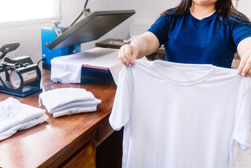 holding white shirts behind a screen printing machine